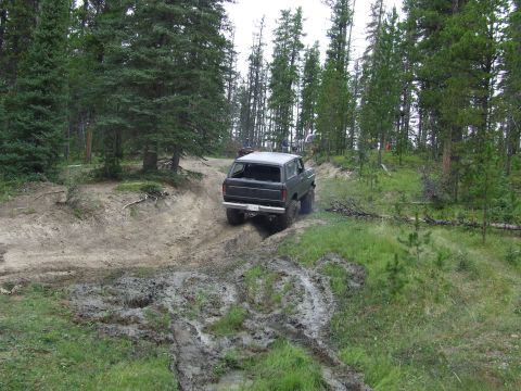 1990 Ford Bronco - A 1990 Ford Bronco navigates a challenging muddy trail in a wooded area.