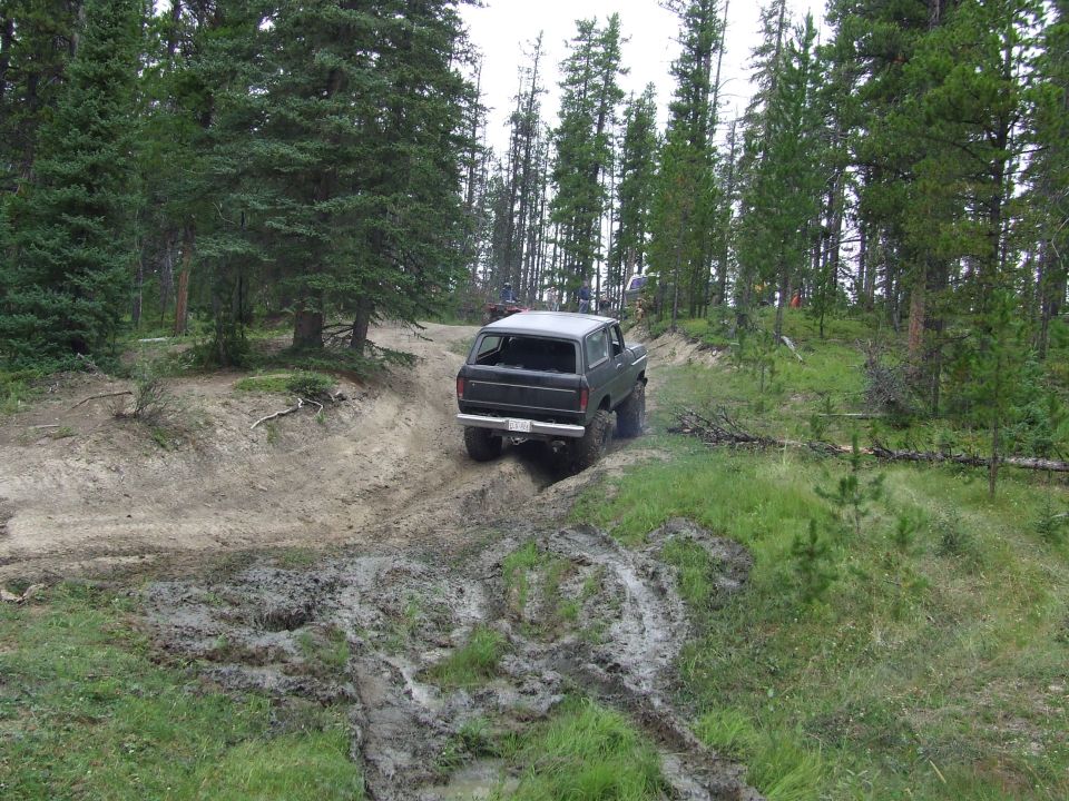 Dark 1990 Ford Bronco driving off-road through mud and trees