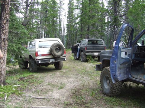 1990 Ford Bronco - Several SUVs, including a 1990 Ford Bronco, are parked on a dirt path in a wooded area.