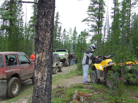 1990 Ford Bronco - A group of off-road vehicles and ATVs are gathered on a trail surrounded by dense forest.