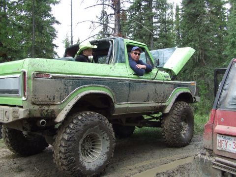 1990 Ford Bronco - Two people in a lifted green Ford Bronco on a muddy trail, with the hood open.