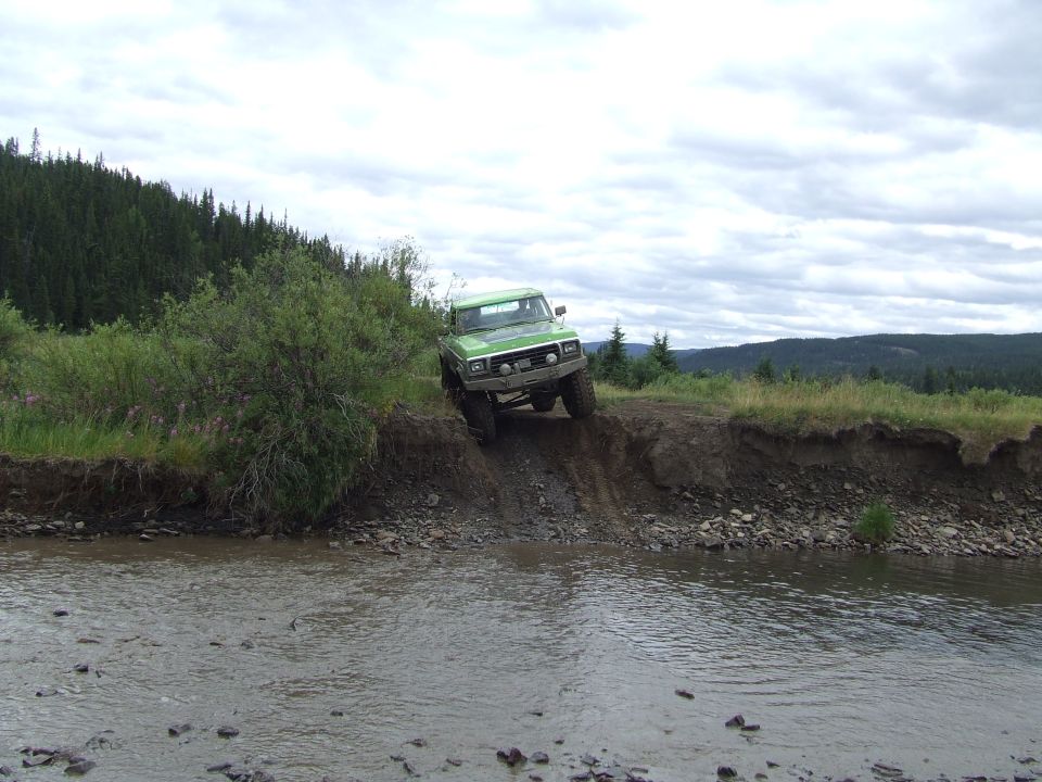 Green truck going down a dirt bank towards a stream
