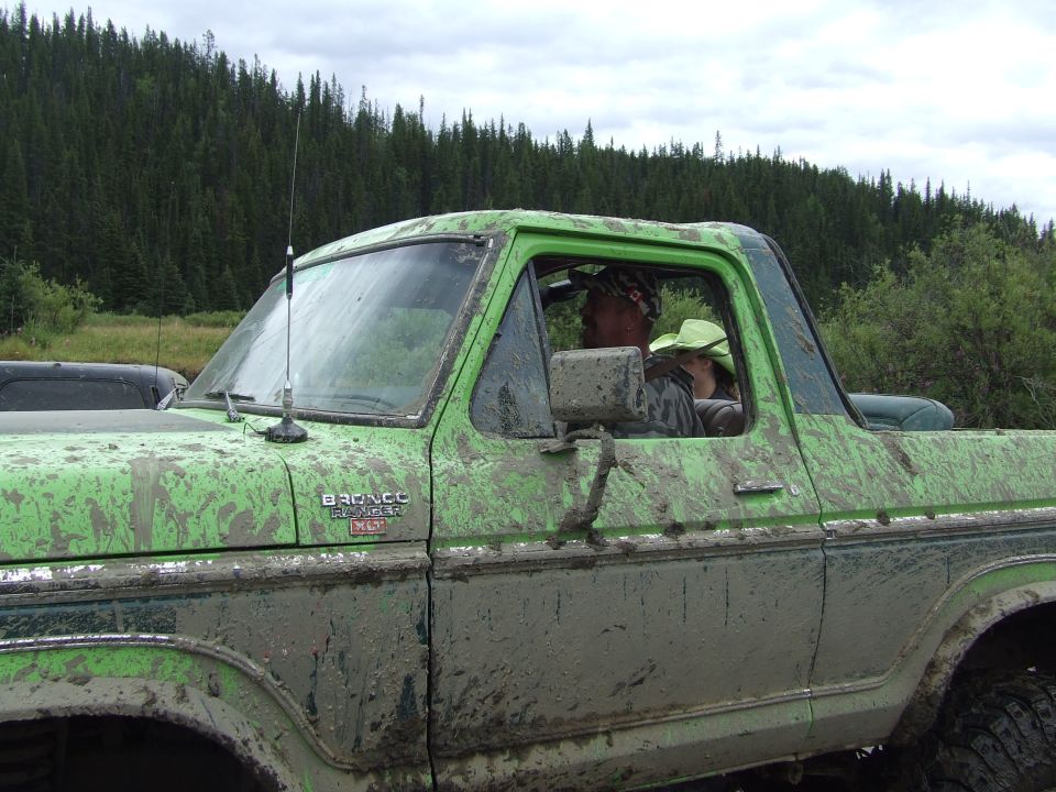 Green Ford Bronco covered in mud, people inside