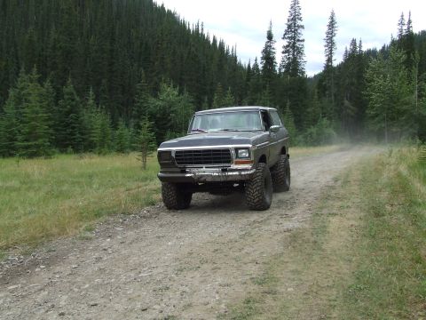 1990 Ford Bronco - This lifted SUV navigates a dusty dirt road through a dense forest landscape.