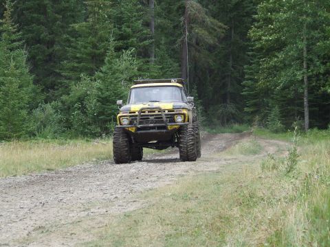 1990 Ford Bronco - A lifted Ford truck with oversized tires navigates a gravel road surrounded by dense pine trees.