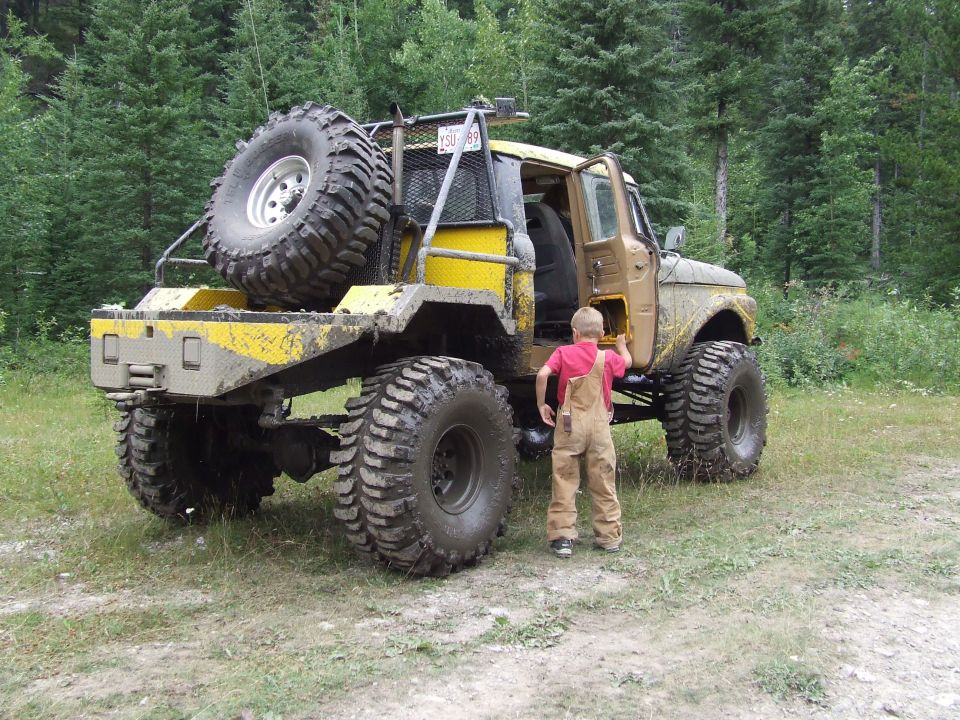 Yellow and tan modified truck with large tires, spare tire on back, and a child in overalls