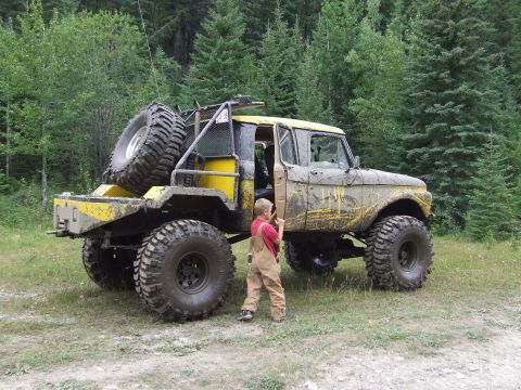 1990 Ford Bronco - A heavily modified pickup truck with oversized tires and a spare tire mounted on the rear is parked in a wooded area.