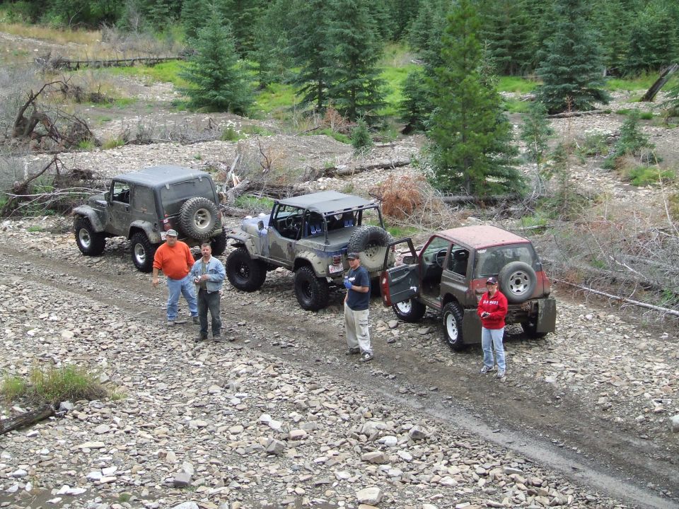 Four off-road vehicles parked on a rocky trail with people standing nearby