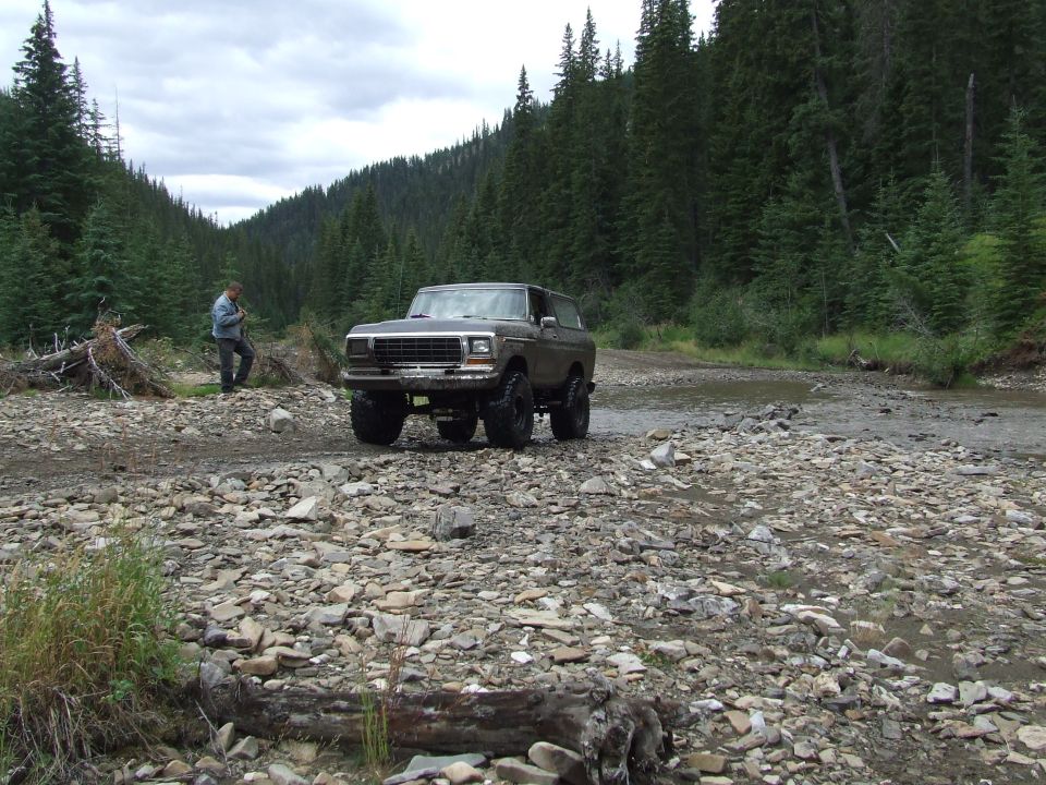 Ford Bronco parked on a rocky stream bed with a person standing nearby
