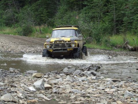 1990 Ford Bronco - Modified Ford F-Series truck navigating a water crossing in a wooded area.