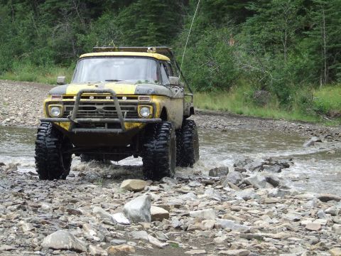 1990 Ford Bronco - This modified Ford pickup truck navigates a shallow, rocky riverbed surrounded by trees.