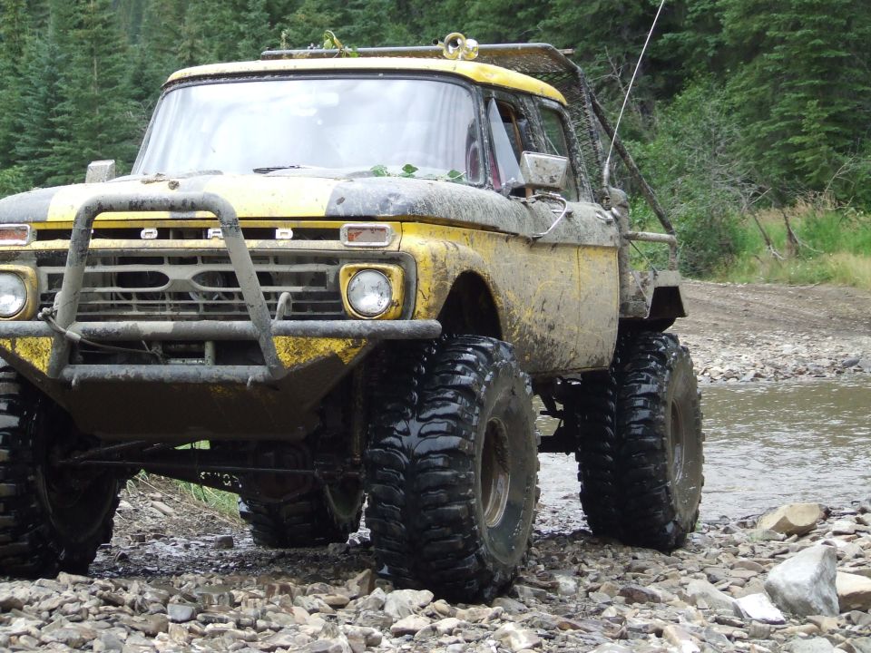 Yellow off-road truck with large tires, mud, and a roll cage