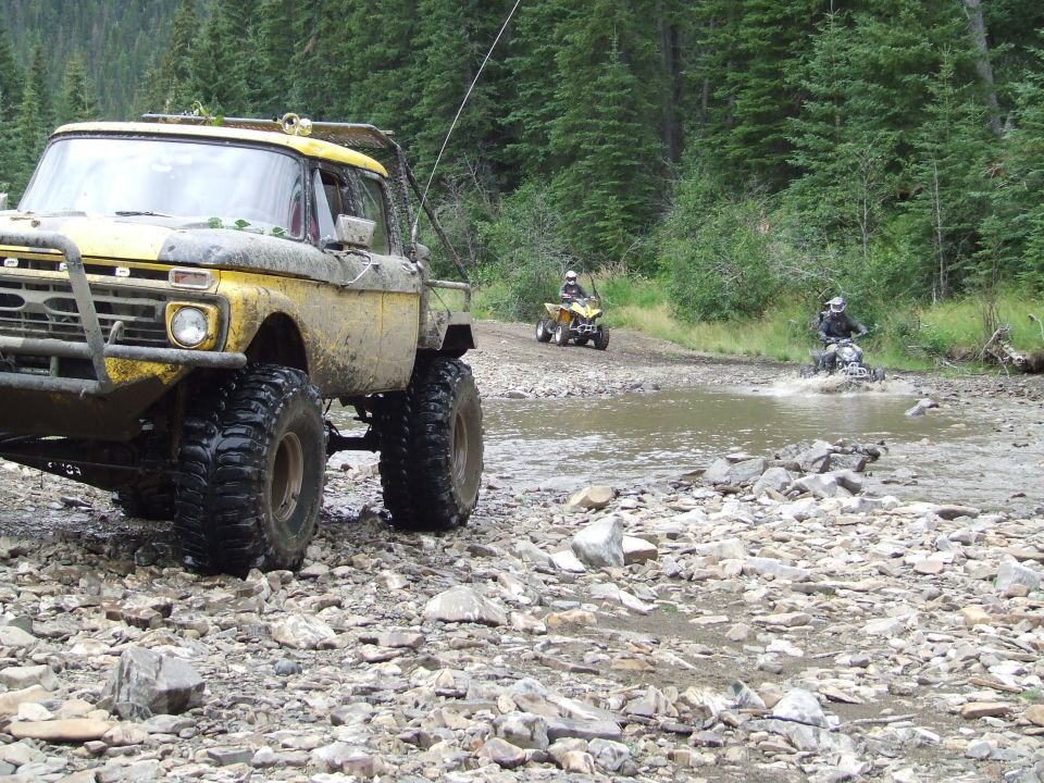 Yellow off-road truck with large tires crossing a rocky stream