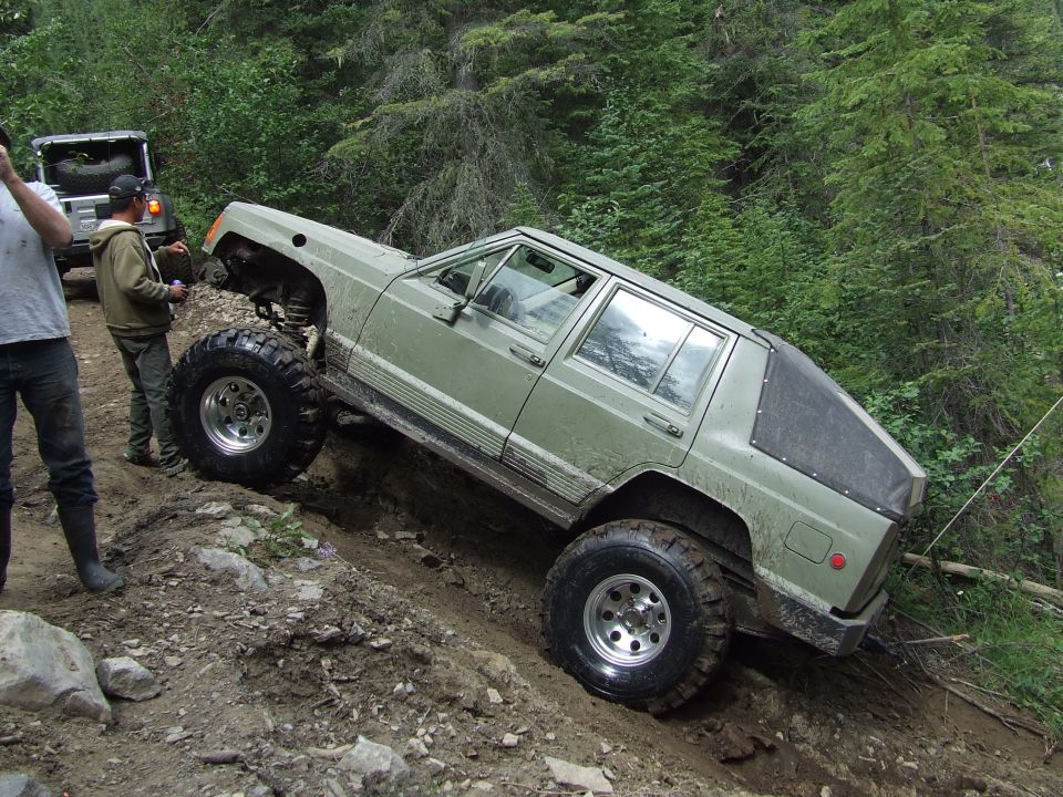 Olive green Jeep Cherokee XJ with large off-road tires navigating a steep dirt trail