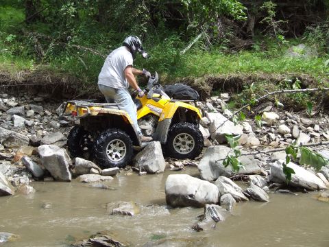 1990 Ford Bronco - ATV rider carefully maneuvers through a rocky stream bed surrounded by dense foliage.