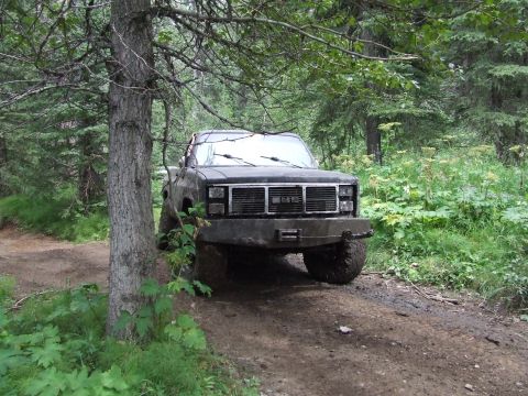 1990 Ford Bronco - A GMC pickup truck navigates a muddy forest trail, surrounded by dense foliage.