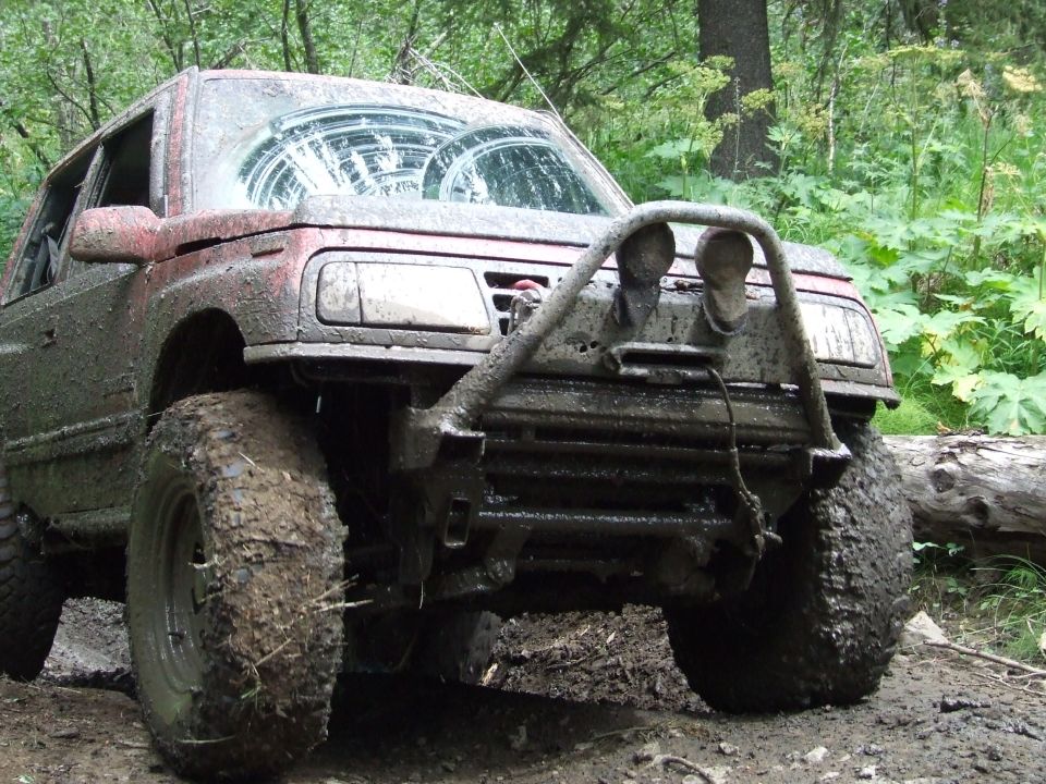 Mud-covered SUV with large tires and a brush guard, parked on a dirt trail