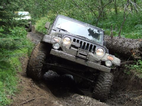 1990 Ford Bronco - A black Jeep Wrangler navigates a challenging, muddy off-road trail, with another vehicle following behind.