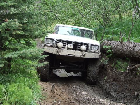 1990 Ford Bronco - Ford Bronco tackling a challenging muddy trail, with a fallen tree obstructing the path.