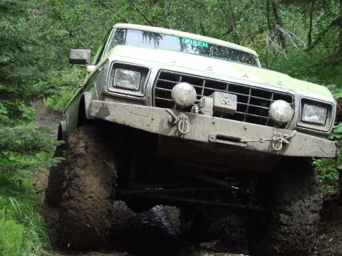 1990 Ford Bronco - This light green Ford truck is navigating a muddy, wooded path with its large tires.