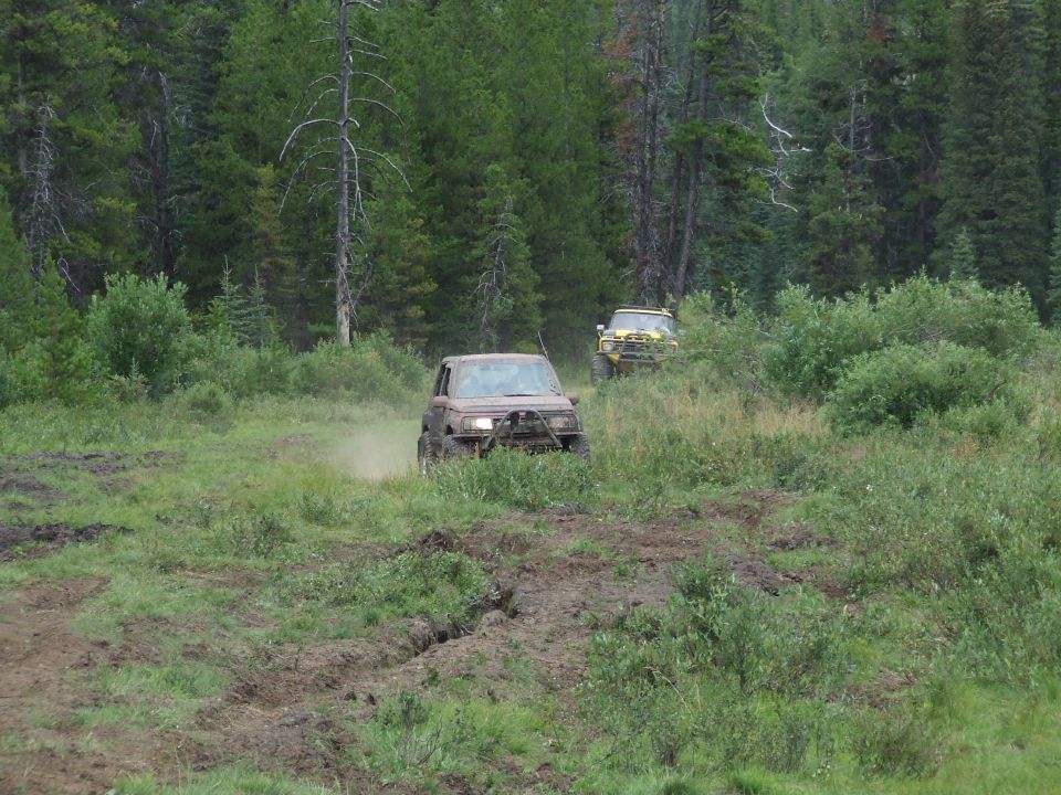 Two off-road vehicles driving on a muddy path through a forest