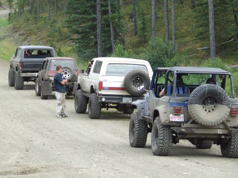 1990 Ford Bronco - A convoy of off-road vehicles, including a 1990 Ford Bronco, travels down a dirt path.