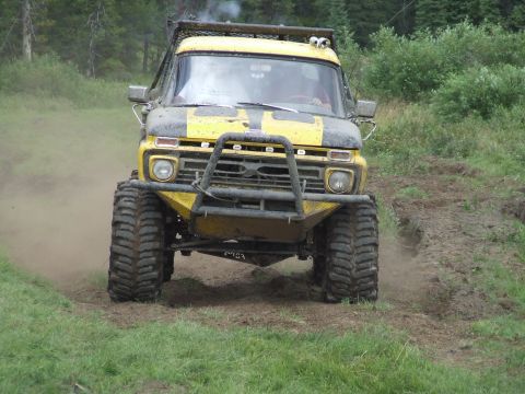1990 Ford Bronco - This modified truck, likely from the 1970s, navigates a muddy trail during an off-road event.