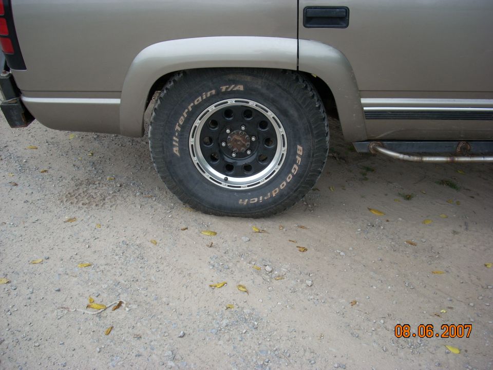 Rear wheel and fender of a tan truck with aftermarket wheels and BFGoodrich tires. A Supermotors watermark is visible