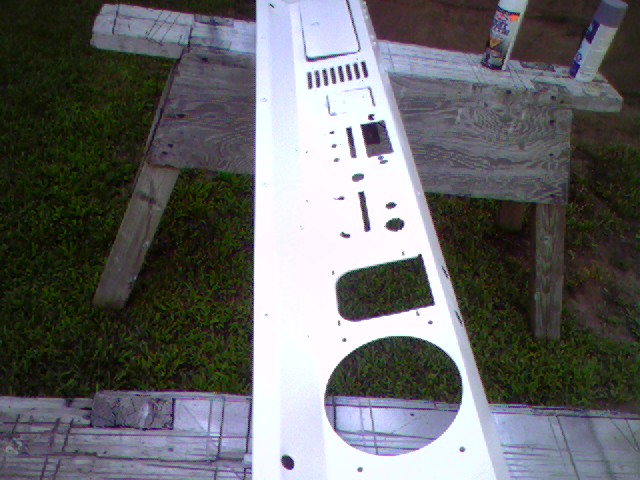 White dashboard panel with various cutouts for gauges and controls, resting on sawhorses outdoors