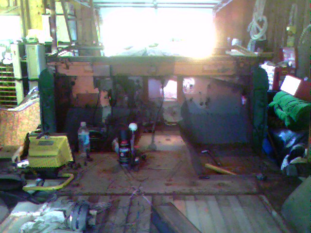 Interior of a garage showing a vehicle chassis with parts scattered around. A yellow tool is on the left