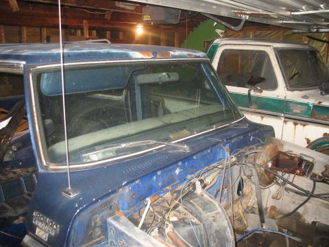1978 Ford Bronco - Two 1978 Ford Broncos are parked indoors, one blue and one white with green trim, both showing signs of wear.