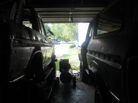 1978 Ford Bronco - Two 1978 Ford Broncos are parked side-by-side in a garage, with the doors open and the vehicles appearing to be under repair.