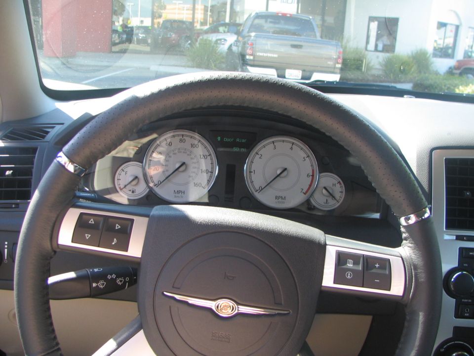 Interior view of a car showing the steering wheel, dashboard gauges, and a pickup truck outside