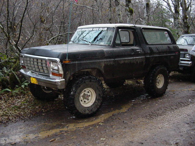 Black and white lifted older Ford Bronco on a muddy forest road, club decal on windshield