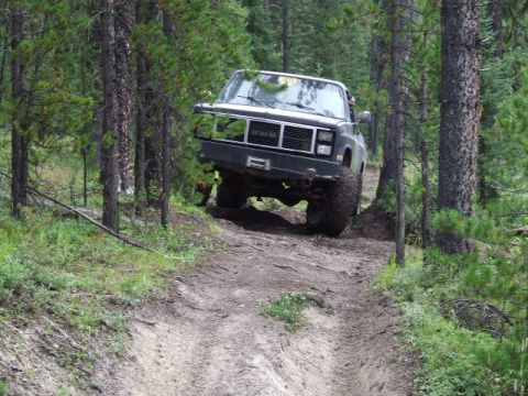 1988 Ford Bronco - Truck navigates a muddy, wooded trail. The grille indicates it is likely a GMC from the 1980s.