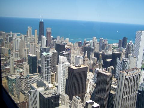 2003 Ford Crown Victoria - A wide shot of the Chicago skyline shows many tall buildings reaching towards the sky, with the blue waters of Lake Michigan visible beyond.