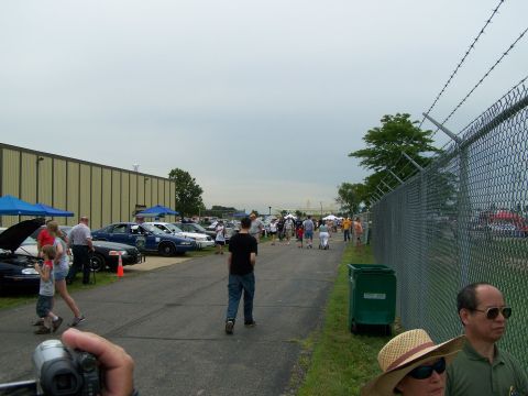 2003 Ford Crown Victoria - An outdoor gathering features several cars parked in rows, with attendees strolling along a paved path.