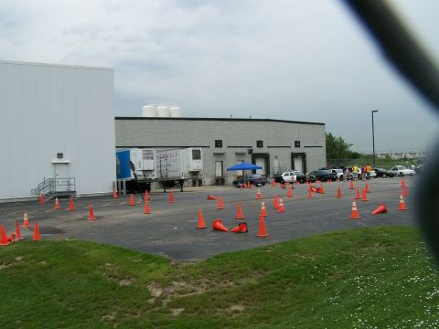 2003 Ford Crown Victoria - A group of vehicles are parked in a lot marked with orange cones, with a large building in the background.