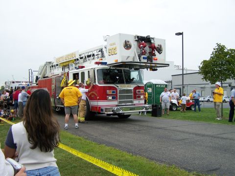 2003 Ford Crown Victoria - A fire truck with its ladder extended is parked on a road, with several people gathered around.