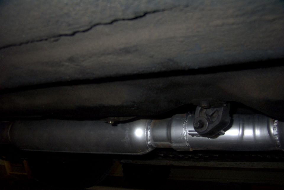 Close-up of a vehicle's exhaust pipe and hanger, with a SuperMotors.net watermark