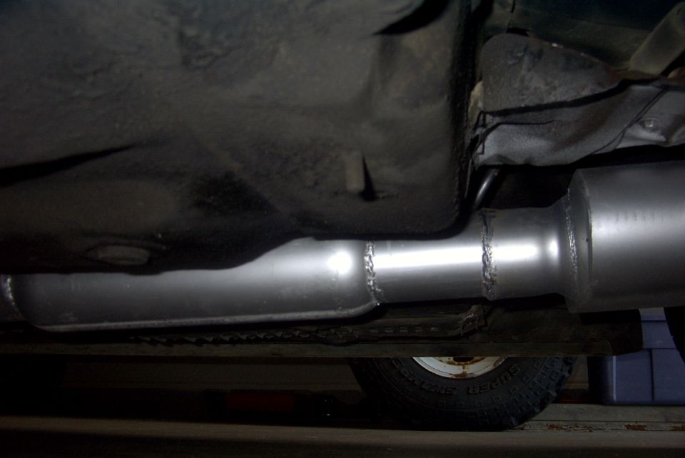 Underside of a vehicle showing a new exhaust pipe and muffler. A tire is visible