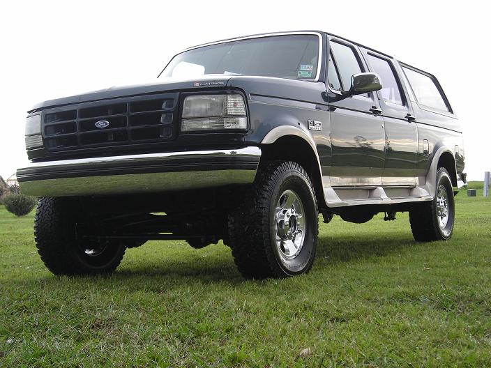 Dark green lifted Ford 4-door SUV conversion, low front 3/4 view on grass