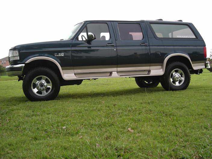 Dark green Ford Centurion crew-cab conversion SUV, side view on grass.