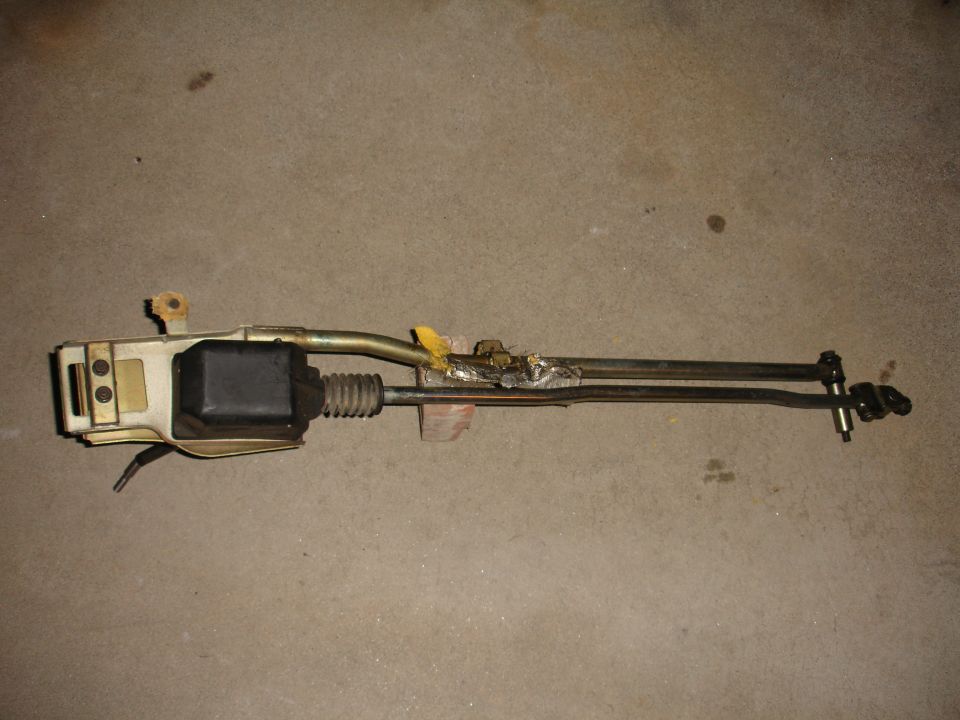 Door latch mechanism with black actuator and metal rods against a concrete background