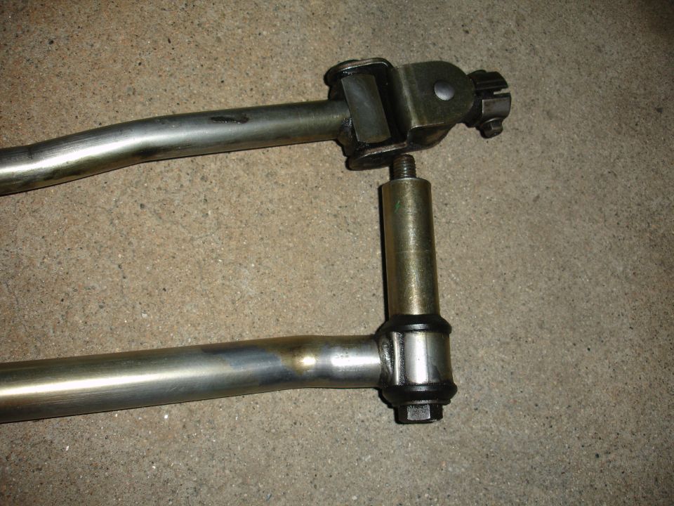 Steering linkage part with metal rods and a jointed connector against a concrete background