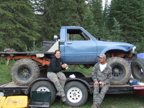 1990 Ford Bronco - A modified blue pickup truck sits on a trailer, with two people nearby in a wooded area.
