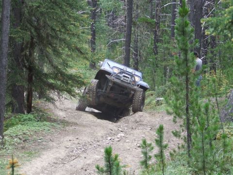 1990 Ford Bronco - A blue 1990 Ford Bronco navigates a steep, wooded trail during an off-road rally.