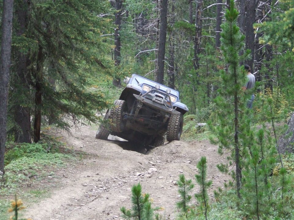 Blue 1990 Ford Bronco on a dirt trail, angled to the left, with large off-road tires and a winch