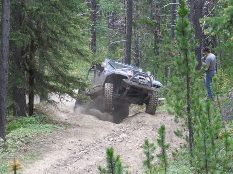 1990 Ford Bronco - A Jeep Wrangler navigates a challenging dirt path during an off-road event in a wooded area.