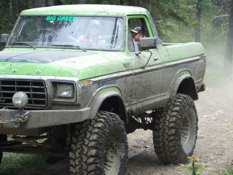 Green Ford Bronco with large tires driving on a dirt road